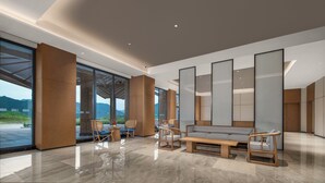 A spacious lobby with a modern design, featuring a large seating area with sofas and chairs, a wooden accent wall, and large windows offering a view of the outdoors.