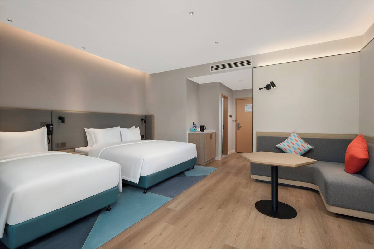 A hotel room with two beds, a sofa, a small table, and a kitchenette area.