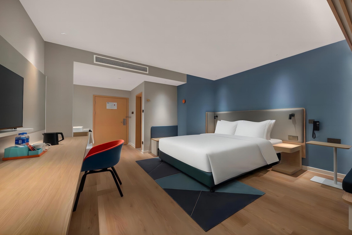 A modern hotel room with a large bed, a desk with a chair, a small seating area, and a telephone.