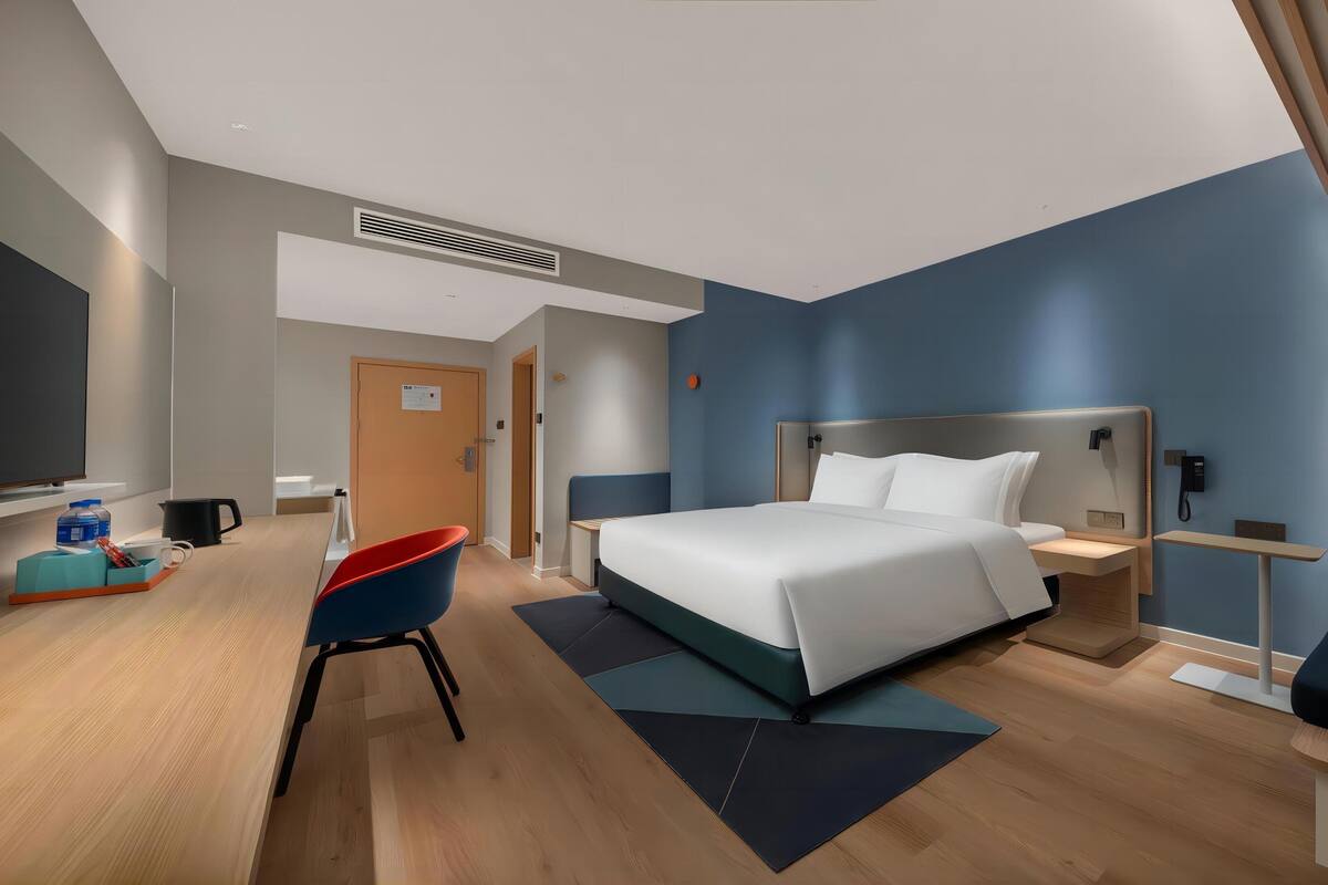 A modern hotel room with a large bed, a desk with a chair, a small seating area, and a telephone.