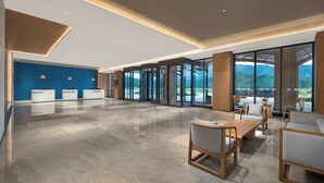 A spacious lobby with a reception desk, seating area, and large glass doors leading to a scenic outdoor view.