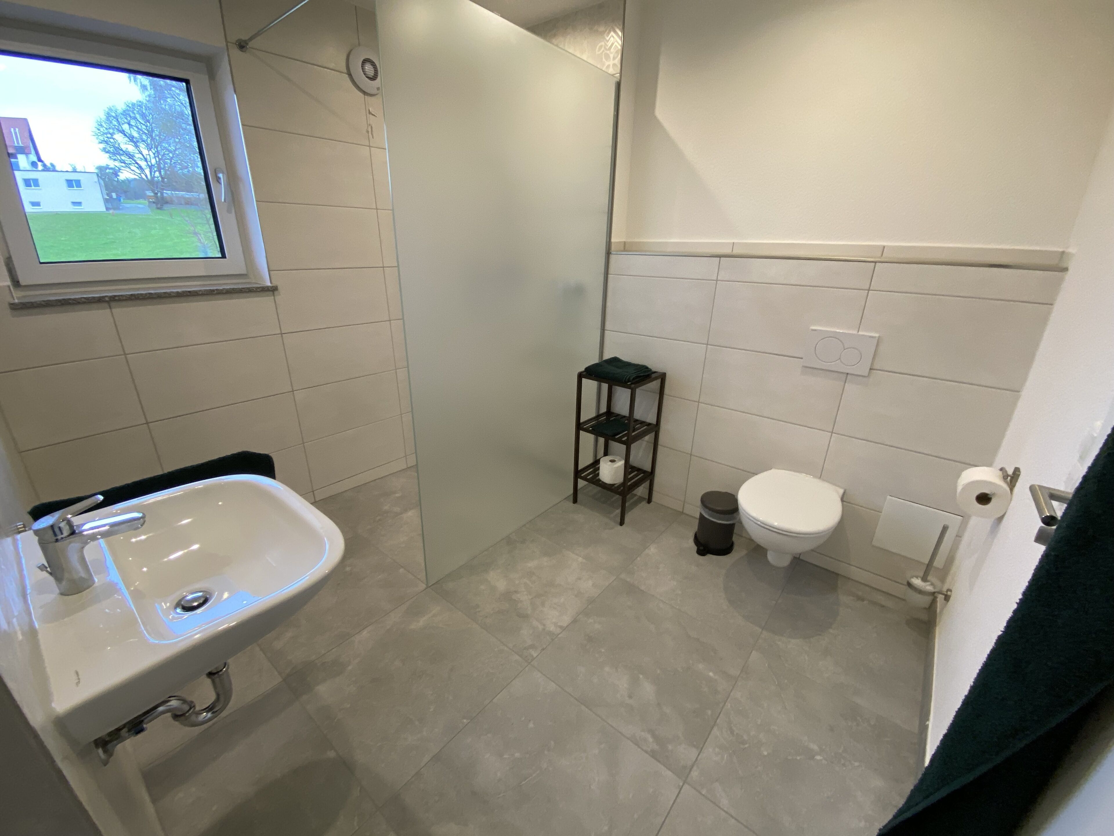 A bathroom with a sink, toilet, and a small shelf with a trash bin.
