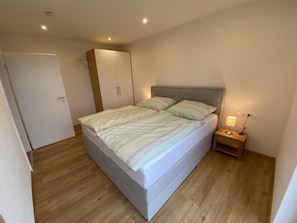 Un dormitorio con cama, mesita de noche, armario y puerta.