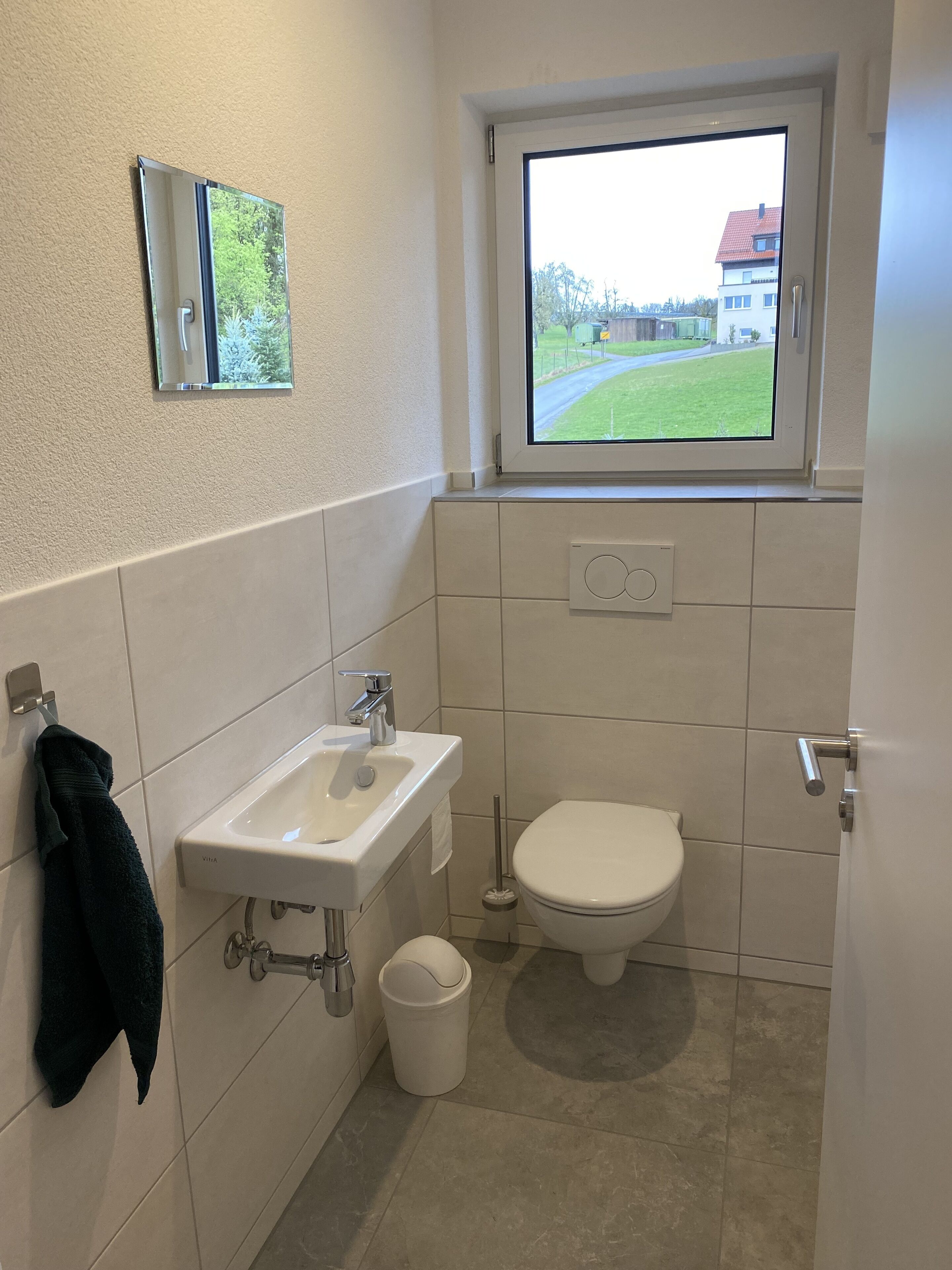 Ein kleines Badezimmer mit Fenster, Waschbecken, Toilette und Mülleimer.