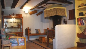 Una habitación rústica con un armario de madera que exhibe cerámica, un banco de madera, una silla blanca con cojín y una estantería con libros.