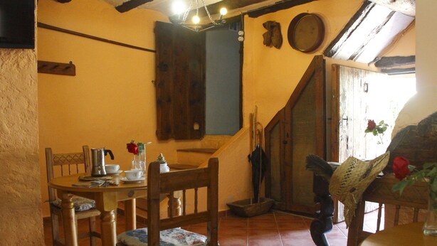 Un comedor con mobiliario de madera, una mesa dispuesta con tetera, tazas y un florero con una flor roja.