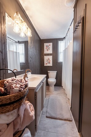 Une petite salle de bain avec un lavabo, des toilettes et un miroir. Des luminaires décoratifs sont placés au-dessus du miroir et un petit tapis recouvre le sol.