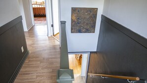 En trætrap med gelænder, der fører op til en platform med en dør og en dekorativt ophængt genstand på væggen.