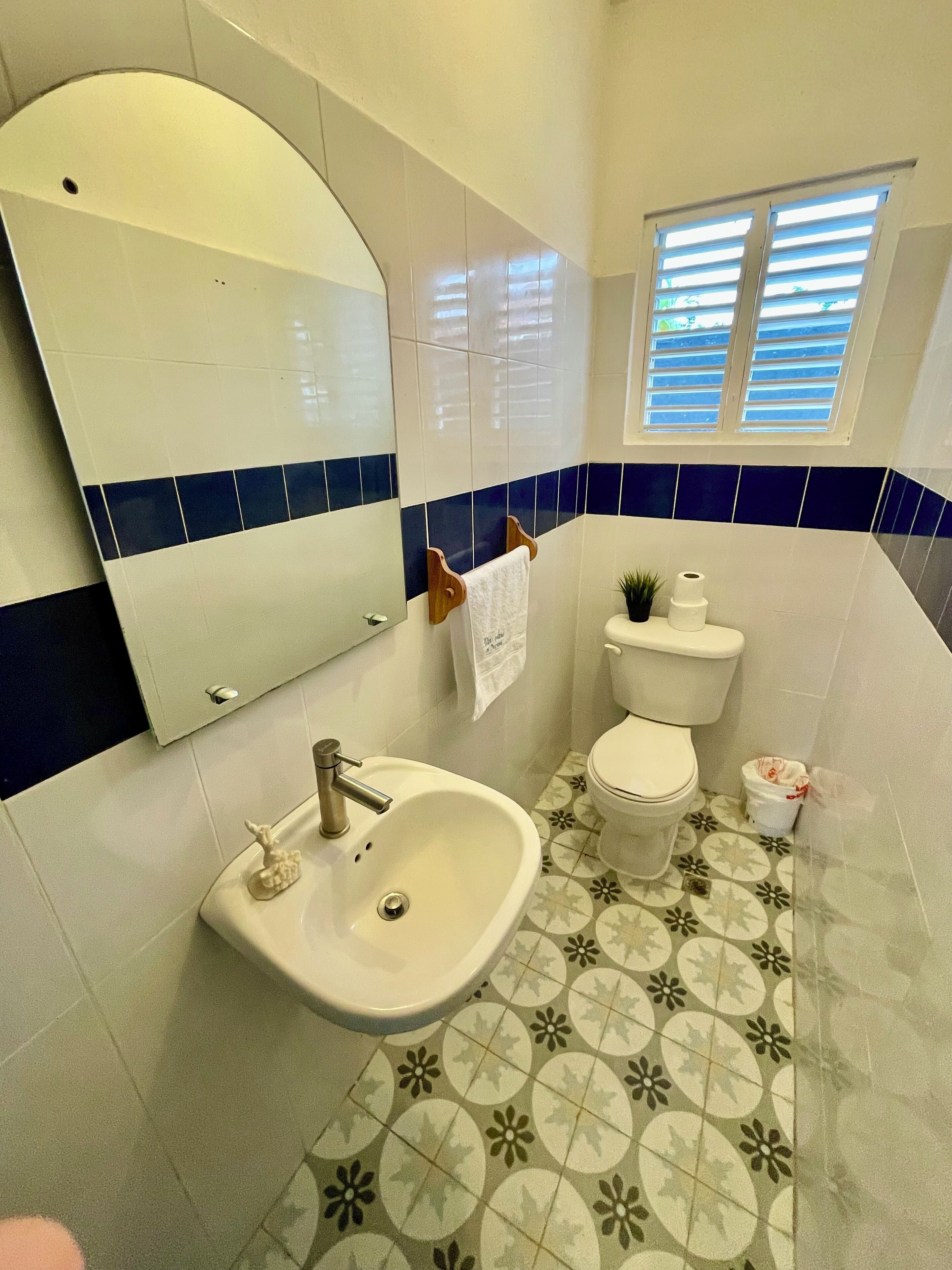 A bathroom with a white sink, toilet, and mirror. The floor has a floral tile pattern.