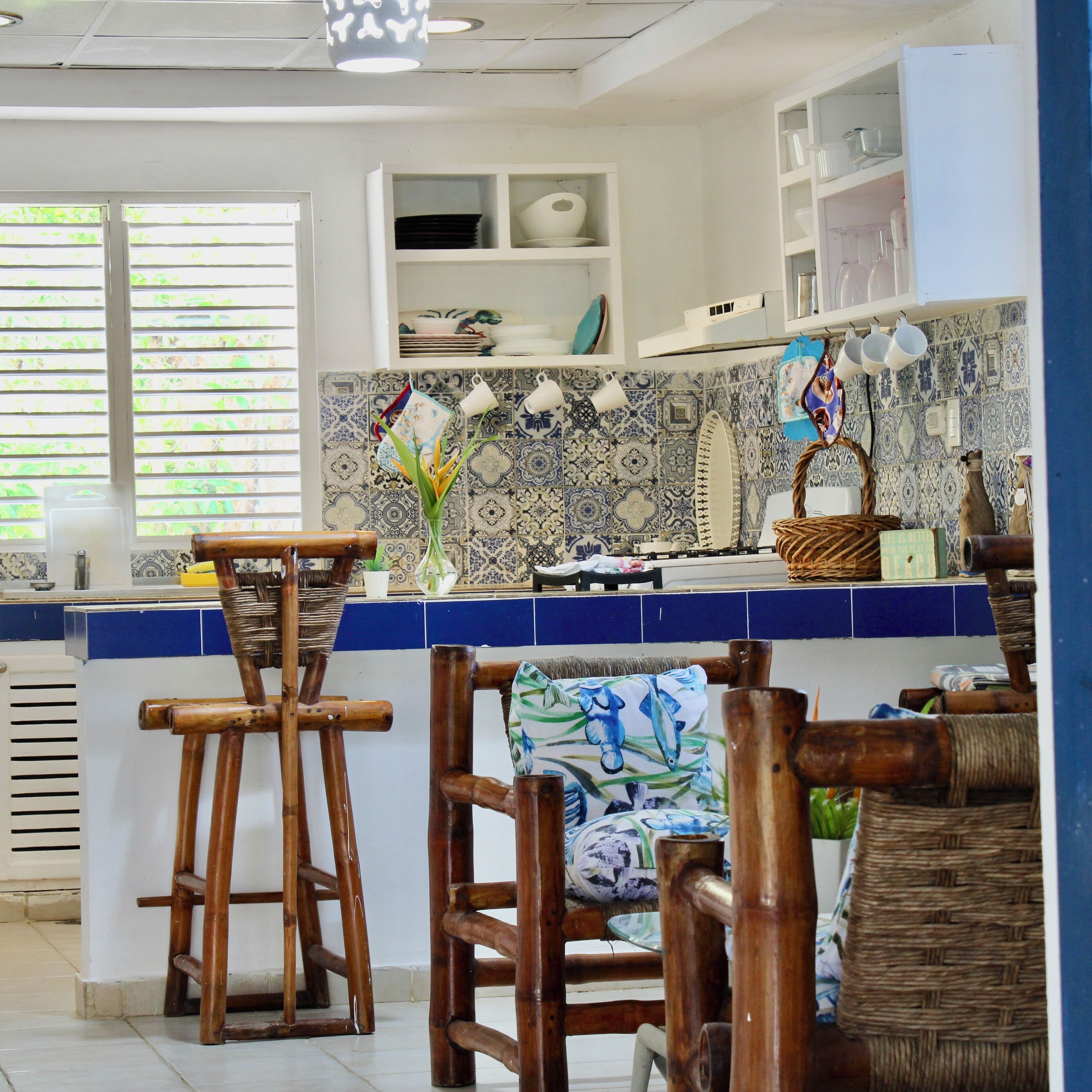 Een keuken met een blauw-wit betegelde spatwand, houten stoelen en een witte koelkast.