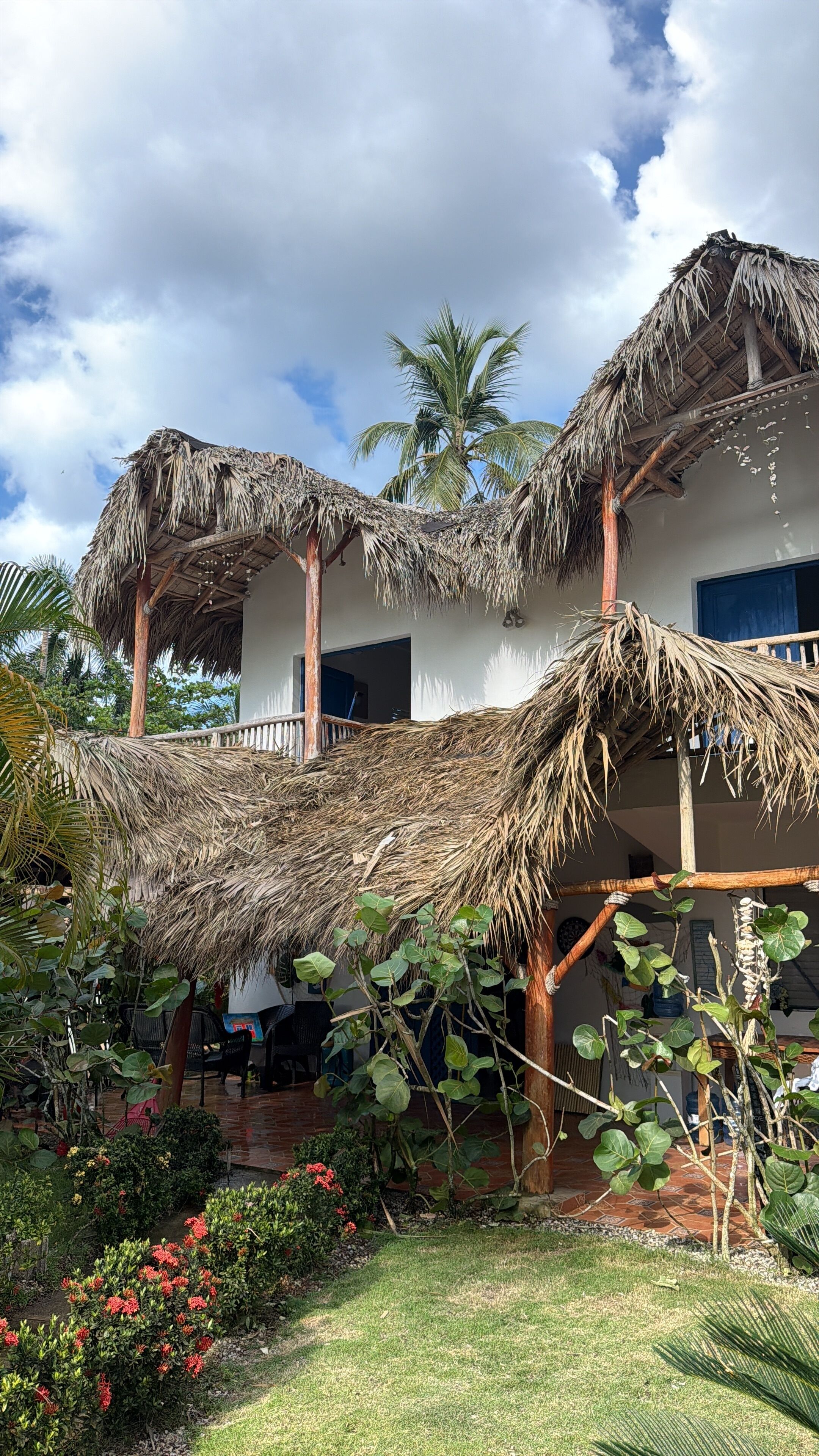 A house with a thatched roof, a balcony, and a garden with tropical plants.