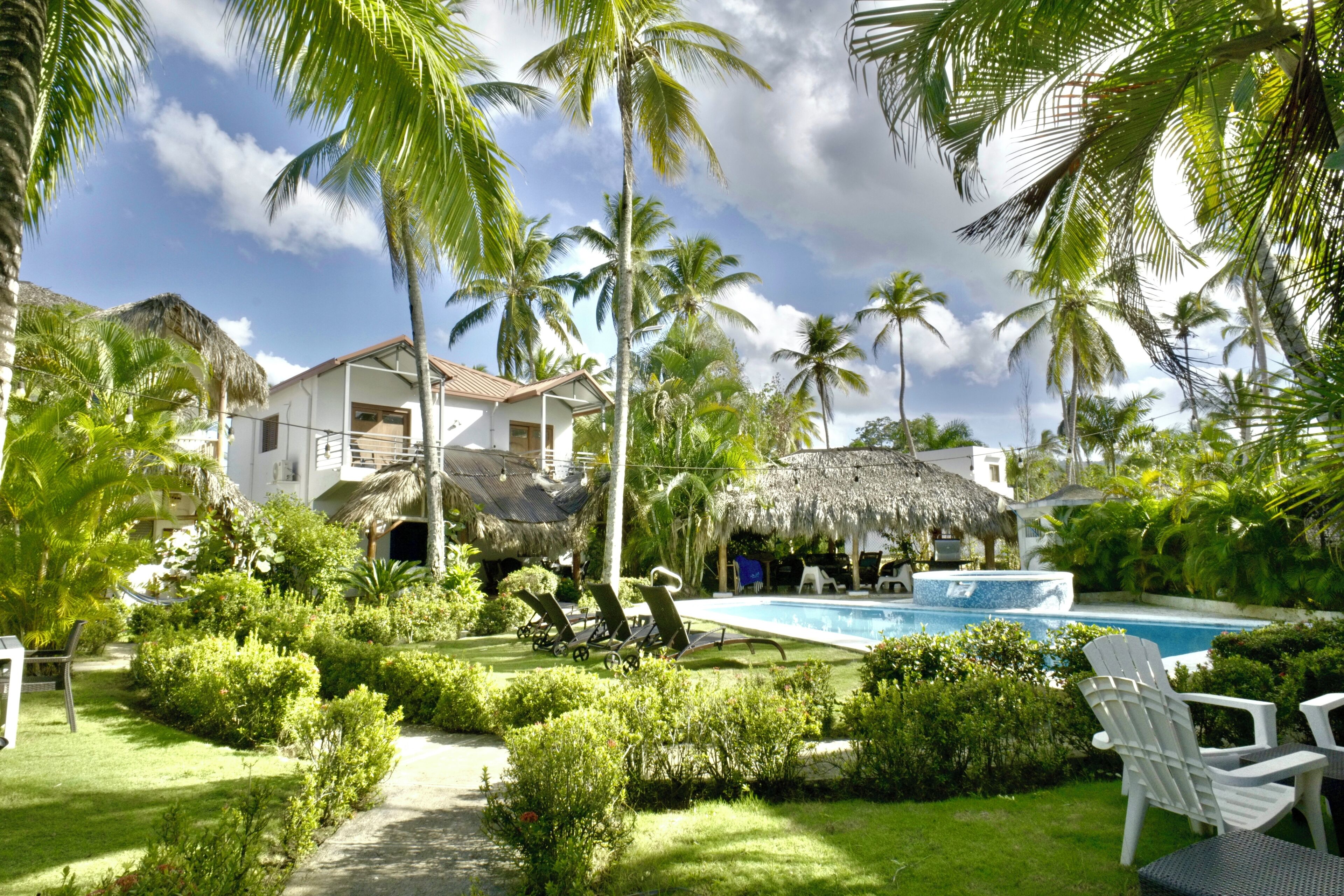 A resort with a pool, palm trees, and a thatched-roof building.