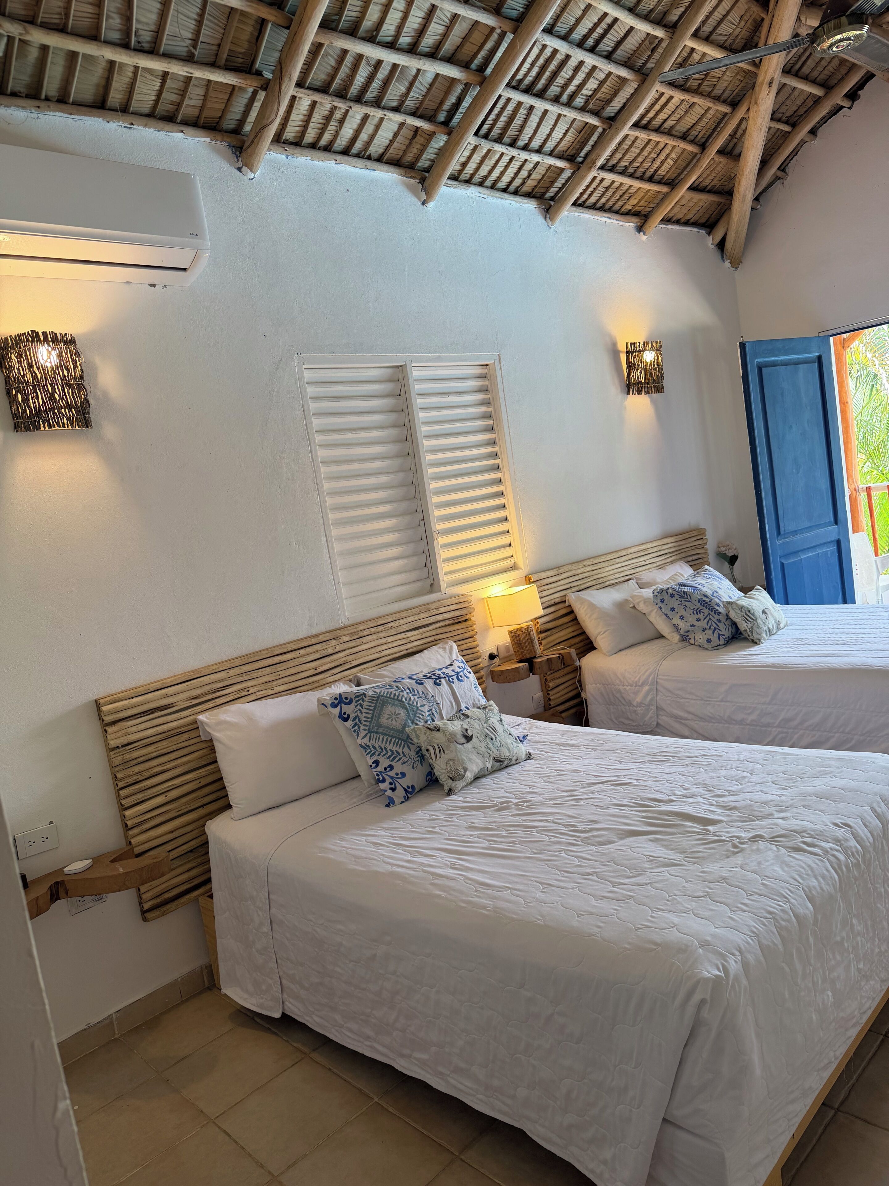 Une chambre avec deux lits, un plafond en bois et une porte bleue.