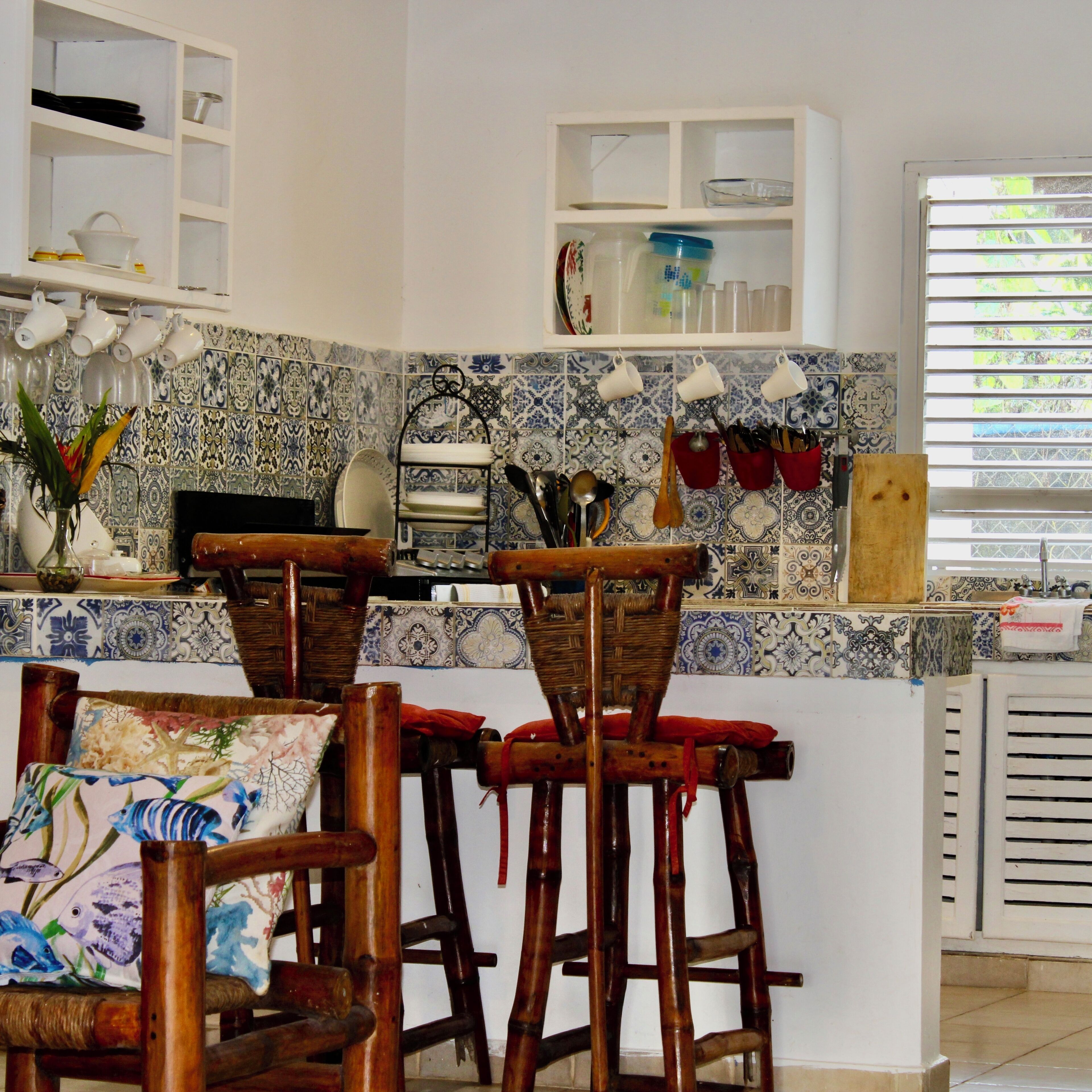 A kitchen with a tiled backsplash, wooden chairs, and a white countertop.
