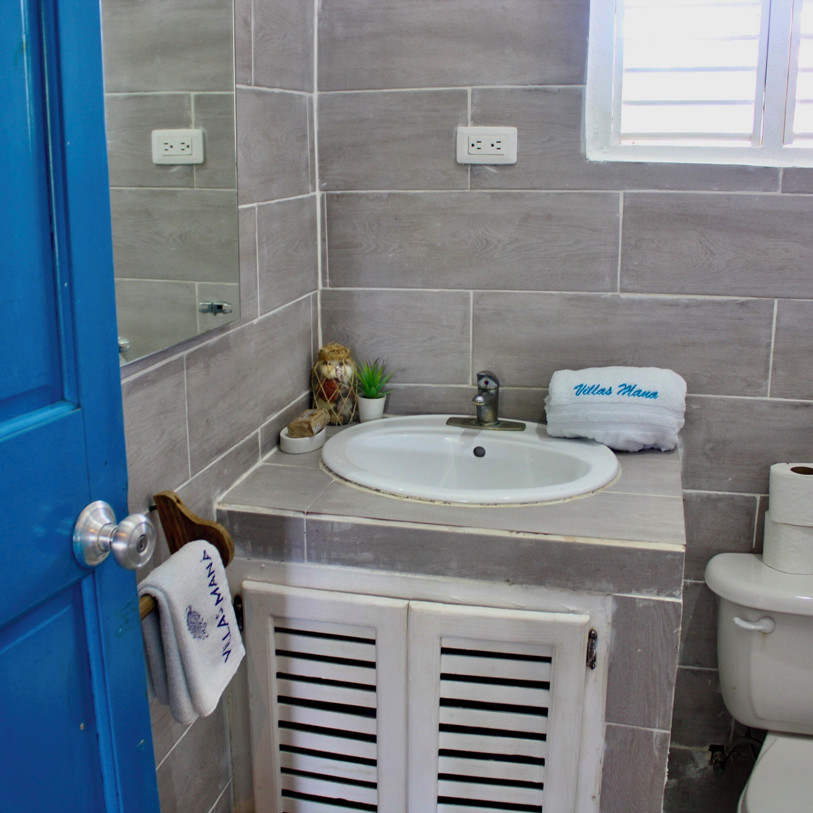 A bathroom with a sink, mirror, and toilet. There is a towel hanging on the door and a small plant on the sink counter.