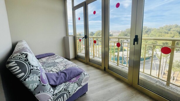 A balcony with a sofa, large windows, and a view of a cityscape.