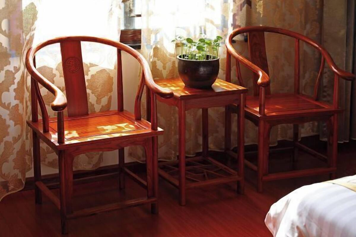Deux chaises en bois, une petite table placée entre elles, une plante en pot sur la table et un lit en arrière-plan.
