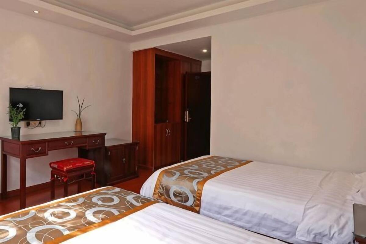 Une chambre d’hôtel avec deux lits, un bureau avec une télévision et une armoire.