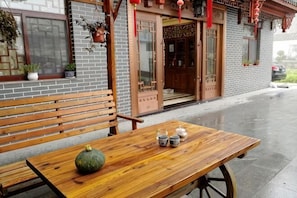 A wooden bench and table with a pumpkin and teapots outside a building with a brick facade and wooden doors.