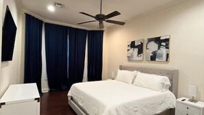 Una camera da letto con un letto, un comodino, una ventola a soffitto e una finestra con tende.