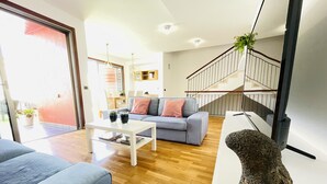 Ett modernt vardagsrum med en grå soffa, ett vitt soffbord och en trappa med ett träräcke.