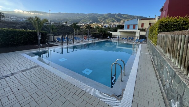 En swimmingpool med solstolar och utsikt över bergen.