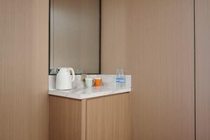 Ein Badezimmer mit einem Holzkosmetikschrank, einem weißen Wasserkocher, einer Tasse und einer Wasserflasche.