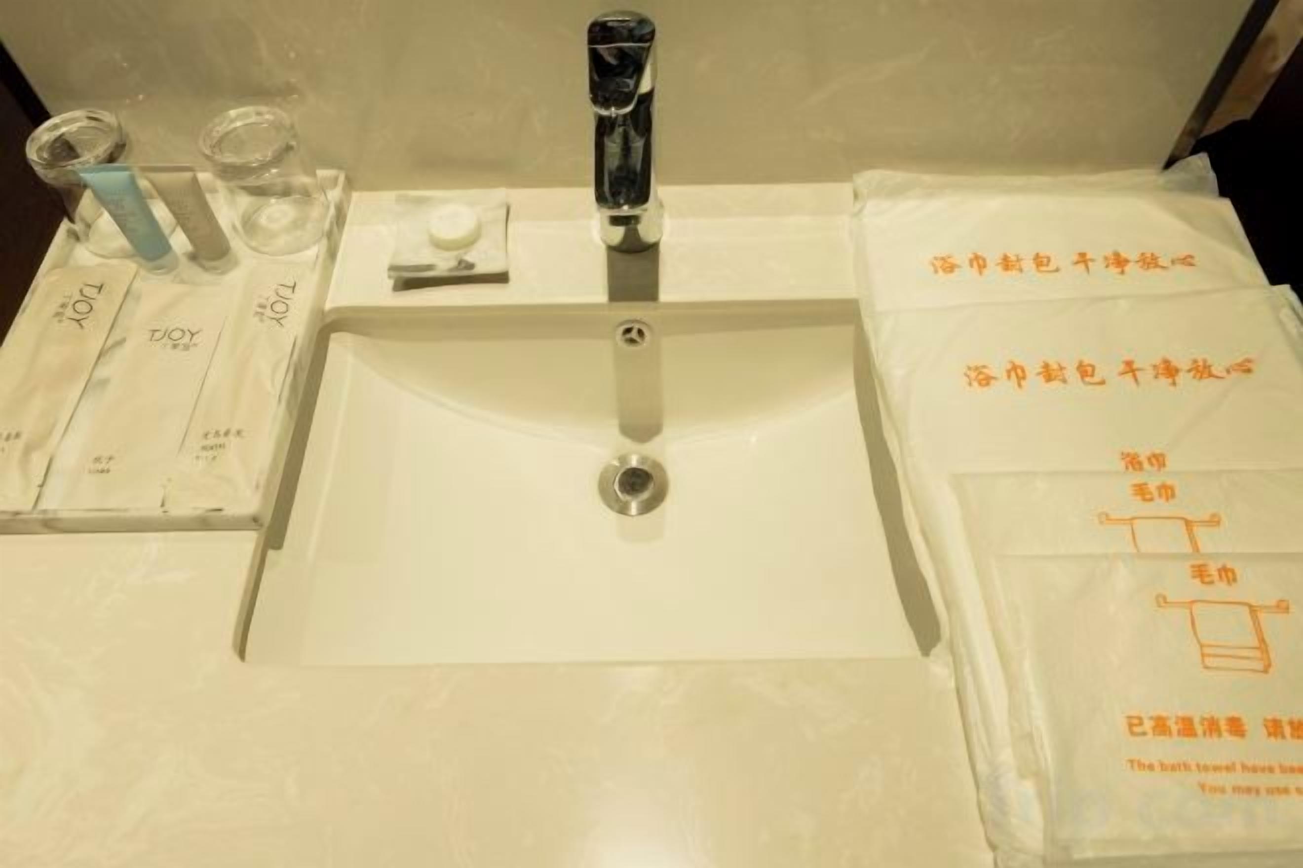A bathroom sink with a faucet, a soap dispenser, and a glass of water. There are also towels and a bag of toiletries on the counter.
