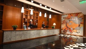 Zona de recepción de un hotel con mostrador de mármol, paneles de madera y un cuadro grande con motivos florales.