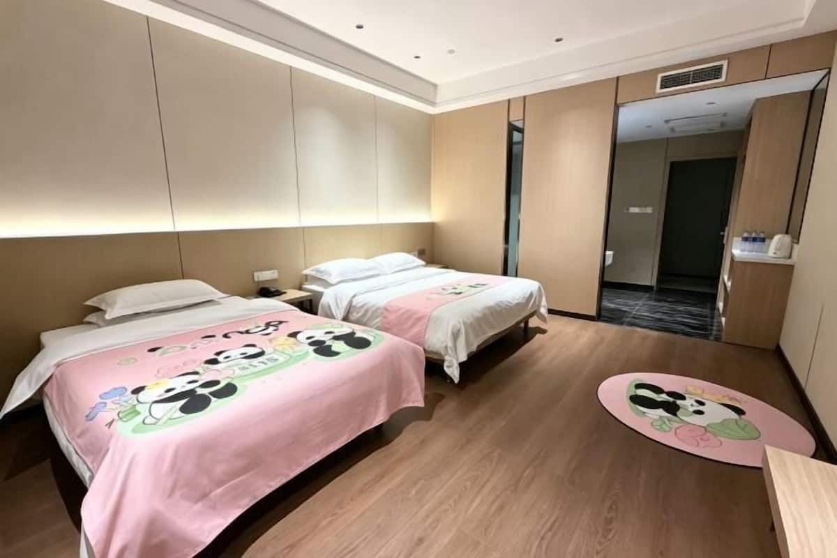 Ein Hotelzimmer mit zwei Betten, Holzboden, Spiegel und einer Tür zum Badezimmer.