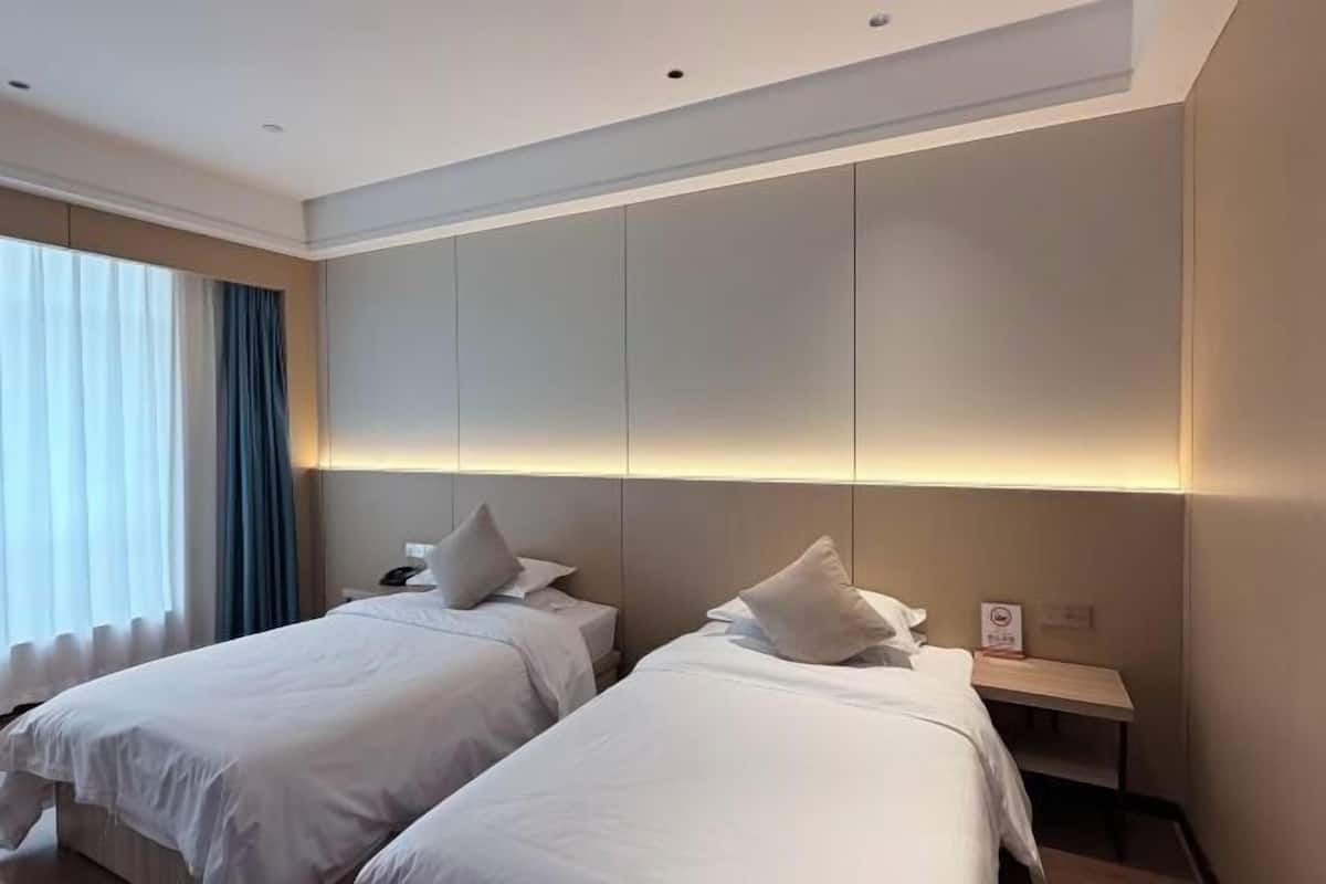 Ein Hotelzimmer mit zwei Betten, einem Nachttisch und einem Fenster mit Vorhängen.