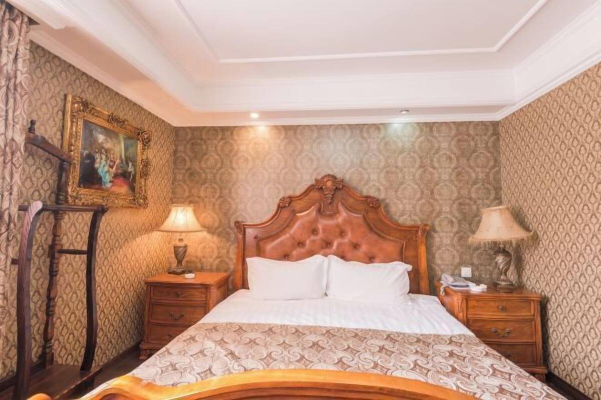 Un dormitorio con cama de madera, papel tapiz estampado y dos mesitas de noche con lámparas.