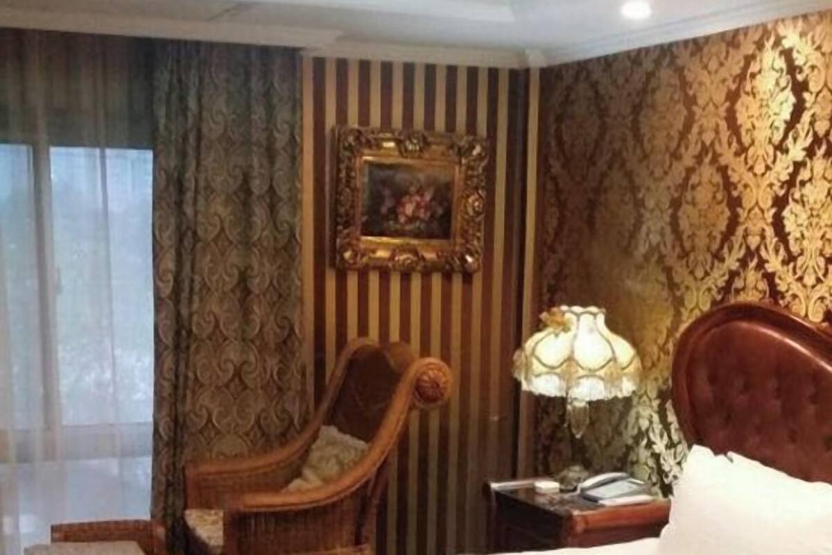 Una habitación de hotel con una cama grande, una silla de madera, una mesita de noche y una lámpara.