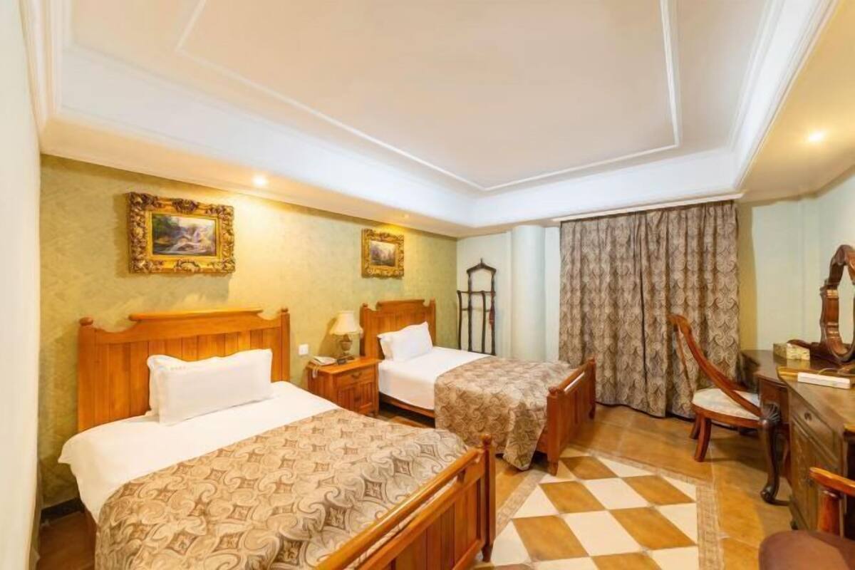 Habitación de hotel con dos camas, un escritorio, una silla y un ventanal con cortinas.