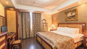 Une chambre d’hôtel avec un grand lit, un bureau avec une chaise, une télévision et une fenêtre avec des rideaux.