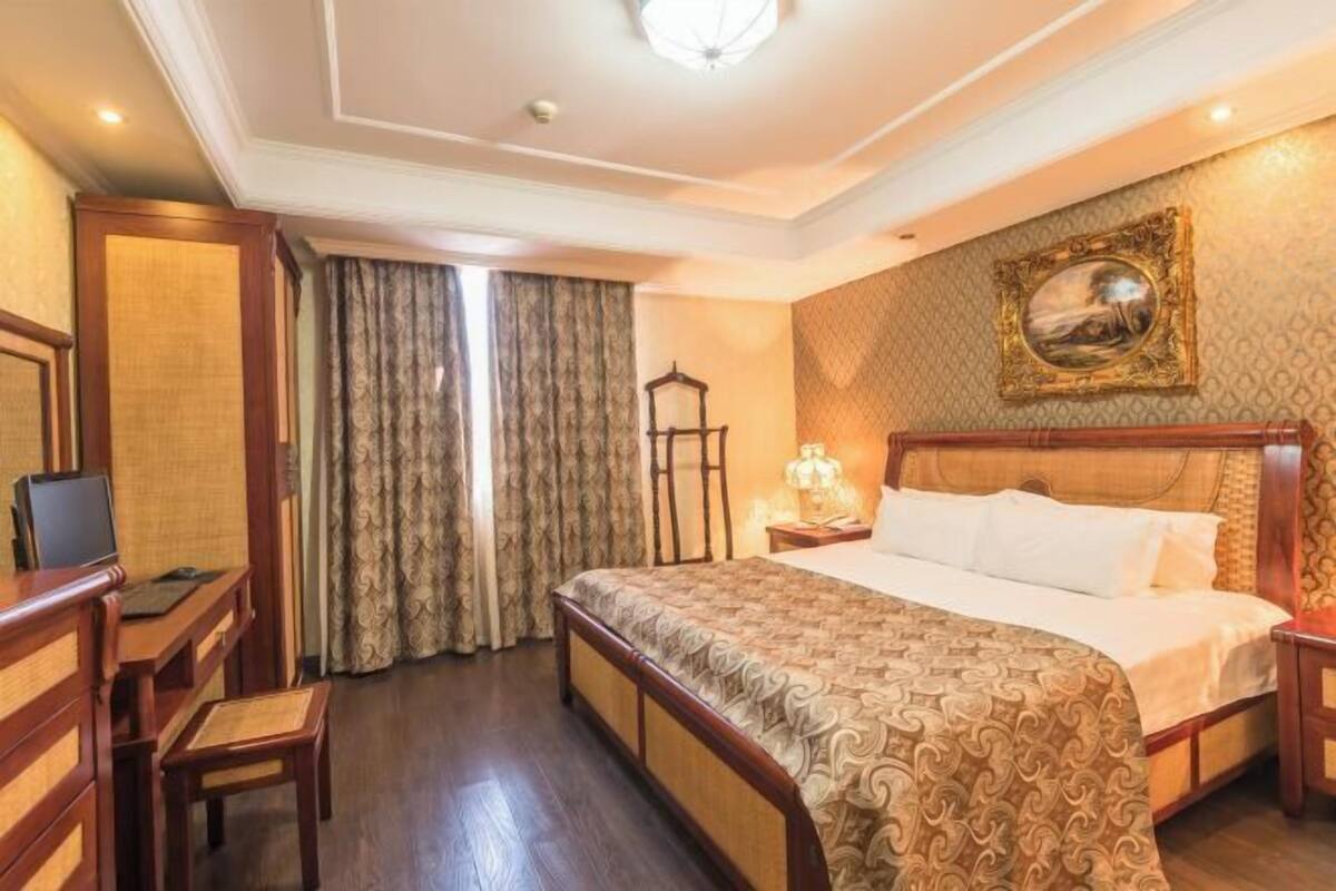 Habitación de hotel con una cama grande, un escritorio con silla, televisión y ventana con cortinas.