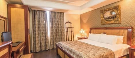 A hotel room with a bed, a desk, a chair, a lamp, and a painting on the wall.