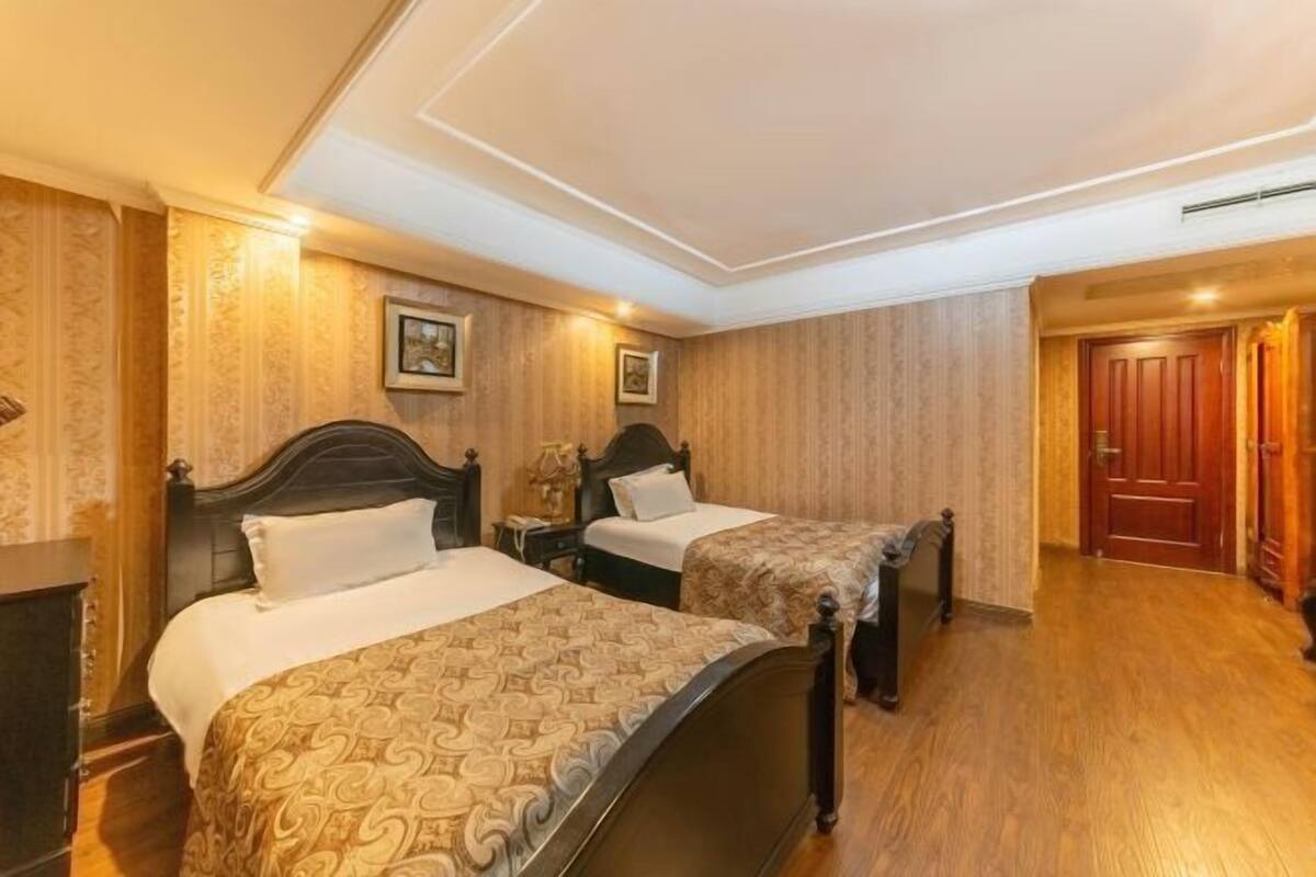 Habitación de hotel con dos camas, suelo de madera y panel de madera en la pared.