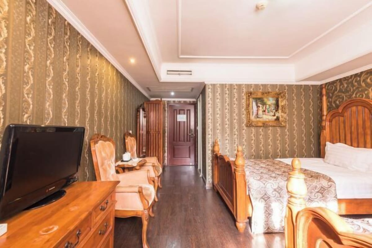 Quarto de hotel com cama, televisão, penteadeira e cadeira.