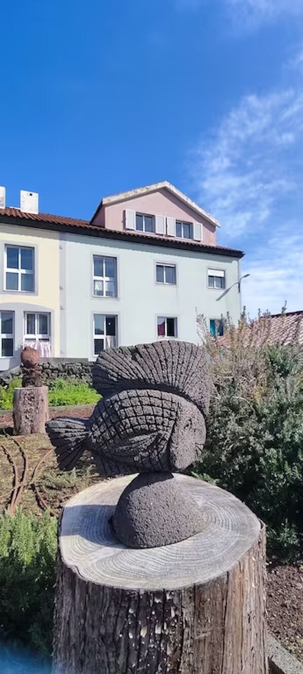 A stone sculpture of a fish on a tree stump in a garden with a building in the background.