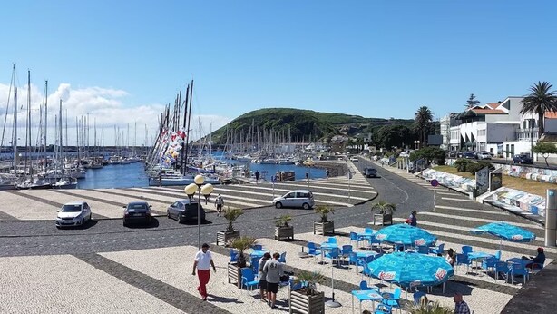Ein Yachthafen mit Booten, einer Fußgängerzone und Außenbestuhlung mit Sonnenschirmen.