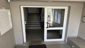 Ein Flur mit einer Treppe, die zu einer oberen Etage führt, einer Tür mit Griff und einer Überwachungskamera an der Wand.