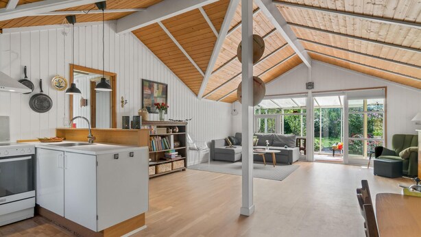 A spacious living area with a kitchen, a dining table, and a large window offering a view of the garden. - 1 bedroom awesome home in Jægerspris (Jægerspris)