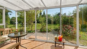 A conservatory with a glass door, a wooden bench, and a table with a vase. - 1 bedroom awesome home in Jægerspris (Jægerspris)