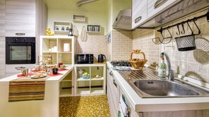 A compact kitchen with a built-in oven, microwave, and gas stove. There are shelves with kitchenware and a small dining area with a table set for two. - 2 bedroom amazing home in Villanova d'Albenga (Villanova d'Albenga)