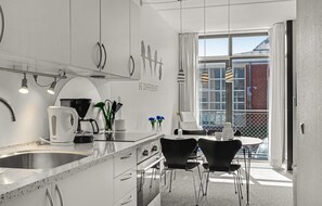 A modern kitchen with white cabinets, a stainless steel sink, and a dining area with two black chairs and a table. - 1 bedroom cozy apartment in Fanø (Fanø)