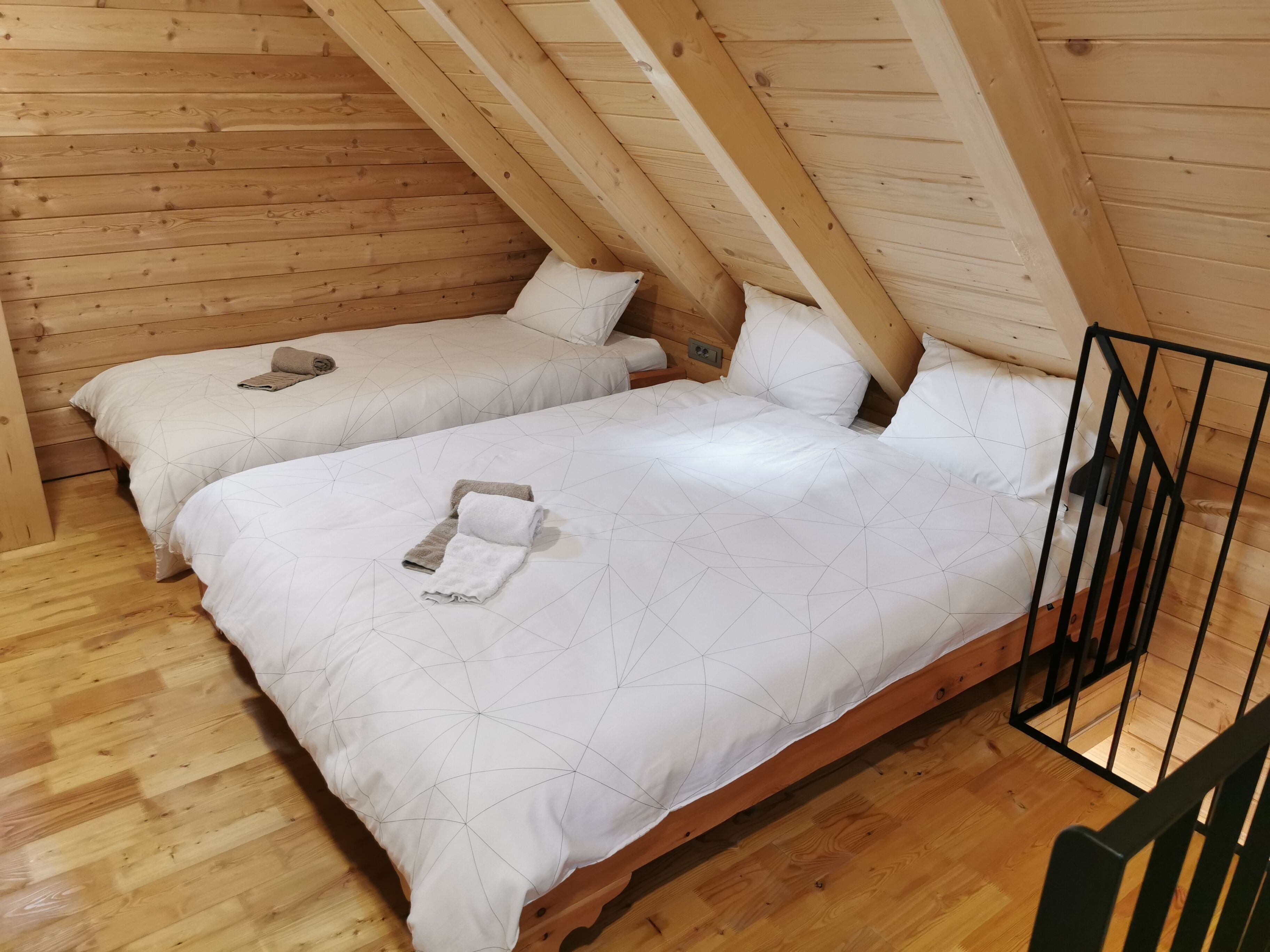 A cozy attic bedroom with two beds, wooden walls, and a sloped ceiling.