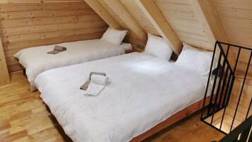 A cozy attic bedroom with two beds, wooden walls, and a sloped ceiling.