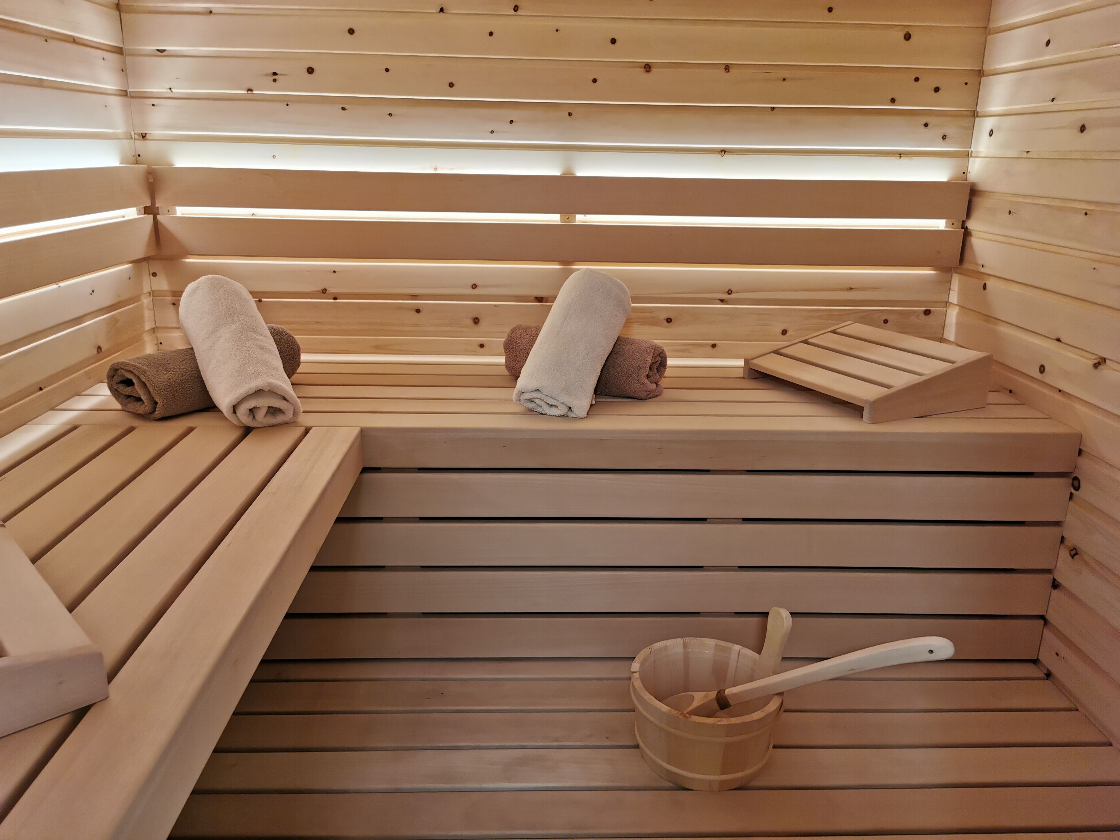 Una sauna con bancos de madera, toallas y un cubo de madera con una cuchara.