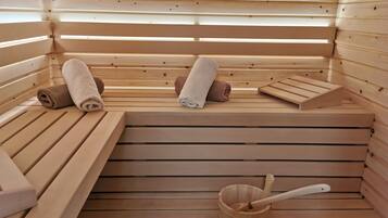 Una sauna con bancos de madera, toallas y un cubo de madera con una cuchara.